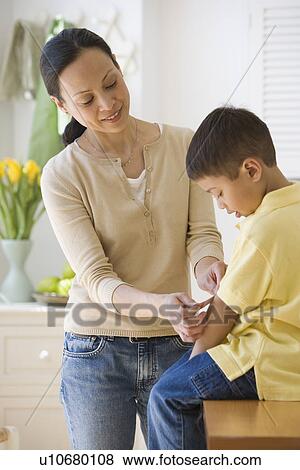 Asian mother putting bandage on son View Large Photo Image Stock Photo - Asian mother putting bandage on son. Fotosearch
