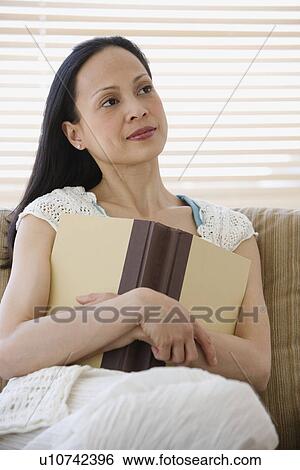 Stock Photograph - Asian woman holding book on sofa. Fotosearch