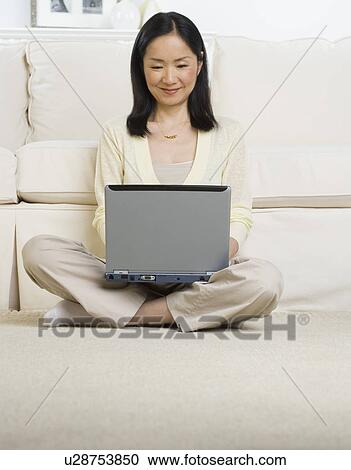Stock Image - Asian woman sitting on floor using laptop. Fotosearch