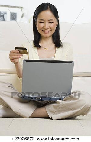 Stock Image - Asian woman with credit card sitting on floor using laptop . Fotosearch