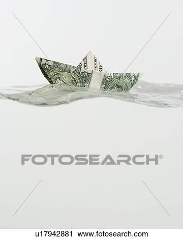 Stock Image - Boat made of US dollar floating on water. Fotosearch