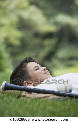 Stock Image - Boy laying in grass with baseball bat. Fotosearch