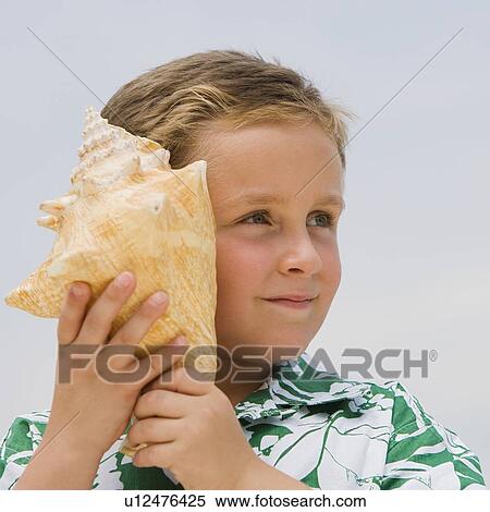 Stock Photography - Boy listening to conch seashell. Fotosearch