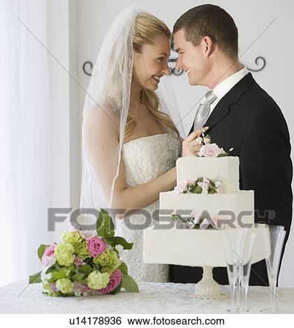 Stock Photograph - Bride and groom next to cake. Fotosearch