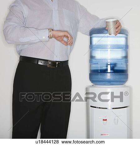 Businessman checking watch next to water cooler View Large Photo Image Stock Photo - Businessman checking watch next to water cooler. Fotosearch