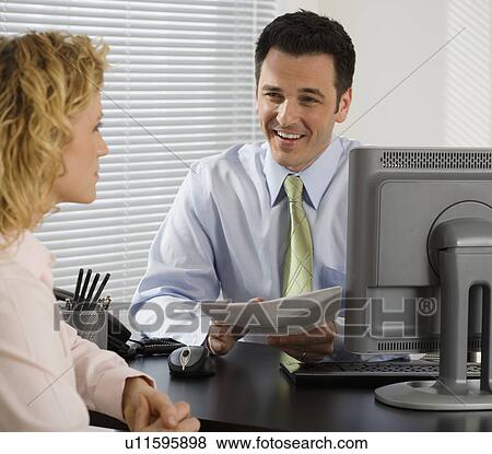 Stock Photo - Businessman consulting with businesswoman at desk. Fotosearch
