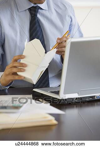 Stock Photo - Businessman eating take out at desk. Fotosearch