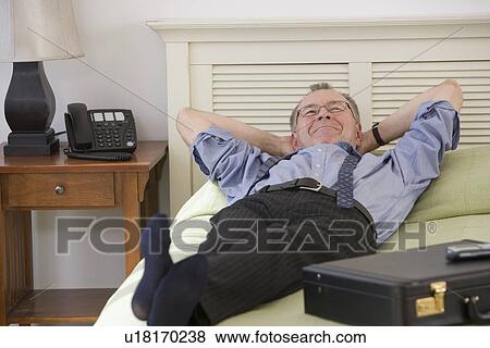 Stock Photo - Businessman laying on bed in hotel room. Fotosearch