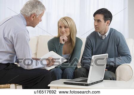 Stock Image - Businessman talking to couple in home. Fotosearch