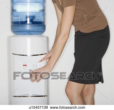 Stock Photo - Businesswoman filling cup at water cooler. Fotosearch