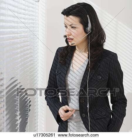 Stock Image - Businesswoman using headset next to window. Fotosearch