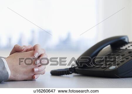 Businesswoman with hands clasped next to telephone View Large Photo Image Stock Photo - Businesswoman with hands clasped next to telephone. Fotosearch