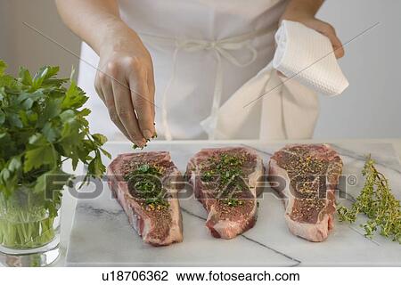 Stock Image - Chef seasoning pieces of meat. Fotosearch
