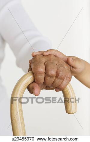 Stock Image - Child's hand laying hand of senior holding cane. Fotosearch