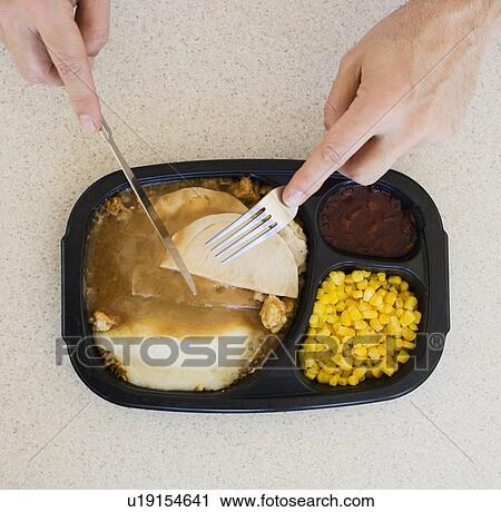 Stock Image - Close up of man eating TV dinner. Fotosearch