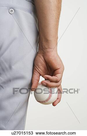 Stock Image - Close up of man holding baseball at side. Fotosearch