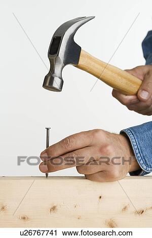Stock Image - Close up of man using hammer and nail. Fotosearch