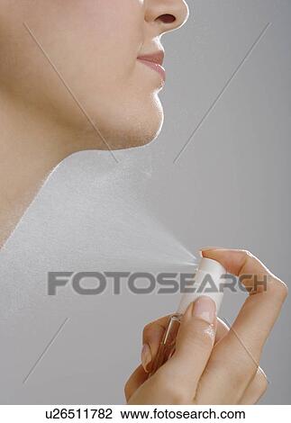Stock Image - Close up of woman spraying perfume on neck. Fotosearch
