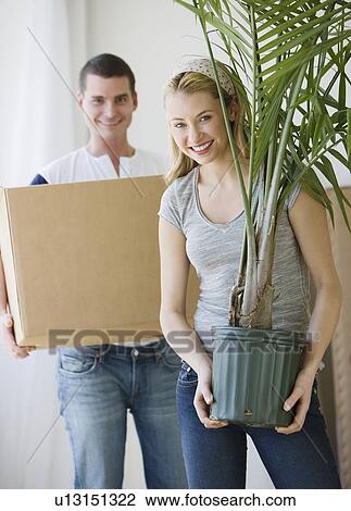 Stock Image - Couple holding moving box and plant. Fotosearch