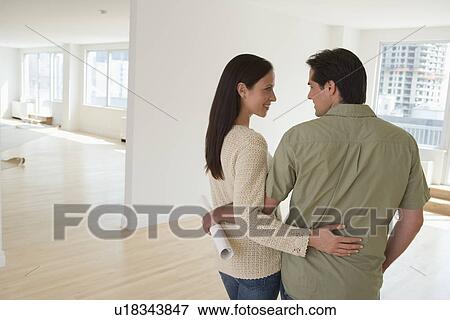 Stock Photo - Couple hugging and holding blueprints in empty house. Fotosearch
