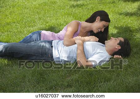 Stock Photo - Couple laying in grass and smiling at each other. Fotosearch