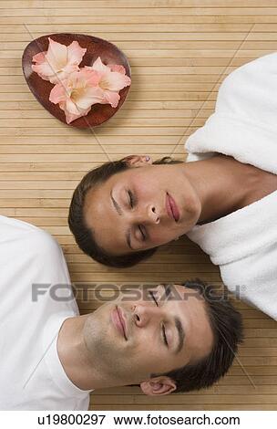 Stock Photo - Couple laying on floor with eyes closed next to flowers. Fotosearch