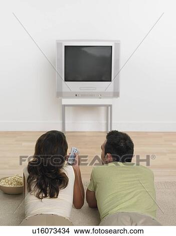 Couple laying on floor with popcorn watching television View Large Photo Image Picture - Couple laying on floor with popcorn watching television . Fotosearch