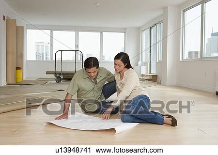 Stock Image - Couple looking at blueprints on floor in new house. Fotosearch