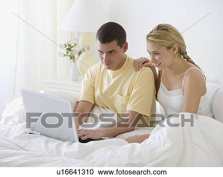 Couple looking at laptop in bed View Large Photo Image Stock Image - Couple looking at laptop in bed. Fotosearch