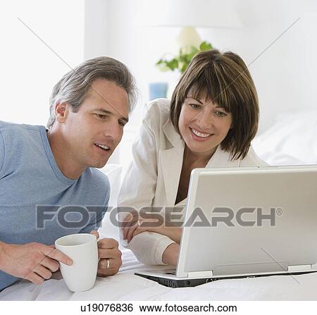 Stock Photograph - Couple looking at laptop on bed. Fotosearch