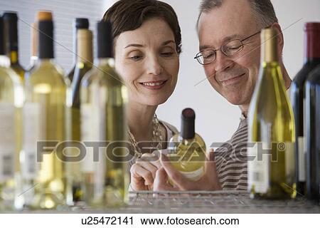 Stock Image - Couple looking at wine in store. Fotosearch