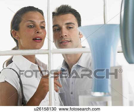 Stock Image - Couple looking through window at vases. Fotosearch