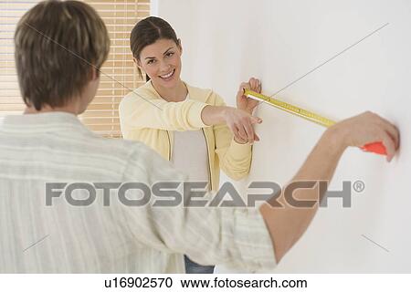 Couple measuring wall with tape measure View Large Photo Image Stock Image - Couple measuring wall with tape measure. Fotosearch
