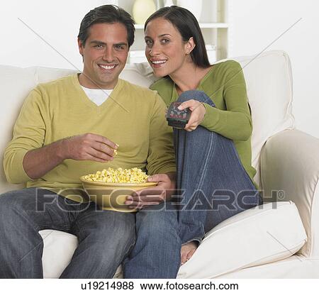 Stock Photo - Couple on sofa with popcorn and remote control. Fotosearch