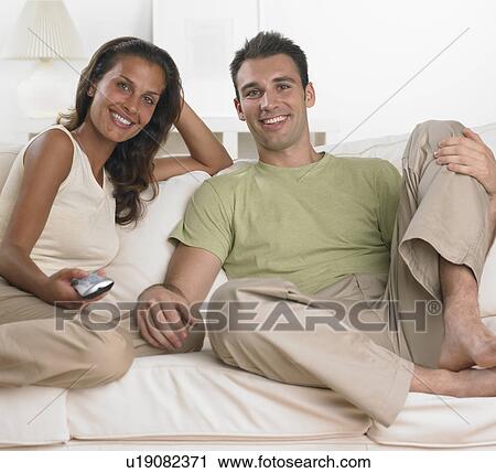 Couple sitting on sofa watching television View Large Photo Image Stock Image - Couple sitting on sofa watching television. Fotosearch