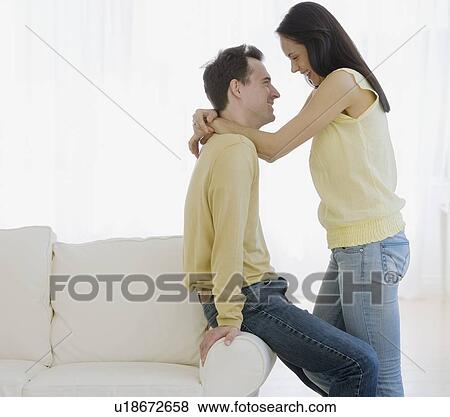 Stock Photo - Couple smiling at each other in living room. Fotosearch