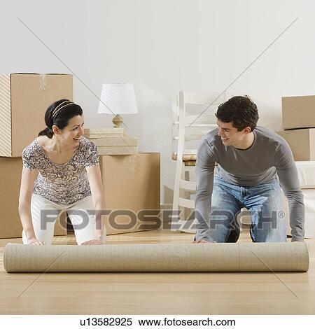 Couple unrolling rug in new house View Large Photo Image Stock Photography - Couple unrolling rug in new house. Fotosearch