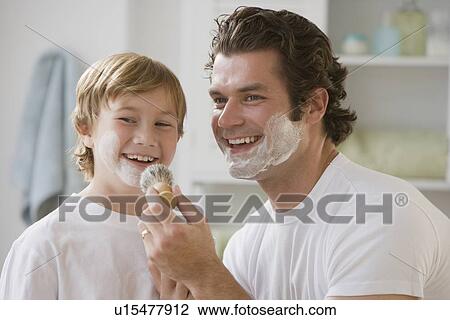 Stock Image - Father putting shaving cream on son’s face. Fotosearch