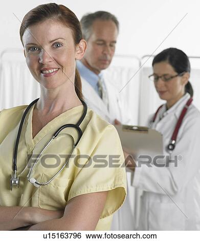 Stock Photograph - Female doctor smiling with doctors in background. Fotosearch