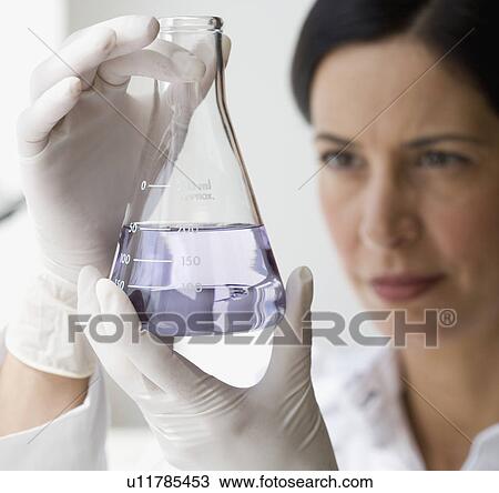 Stock Image - Female scientist looking at liquid in beaker. Fotosearch