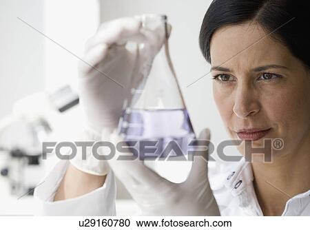 Stock Image - Female scientist looking at liquid in beaker. Fotosearch