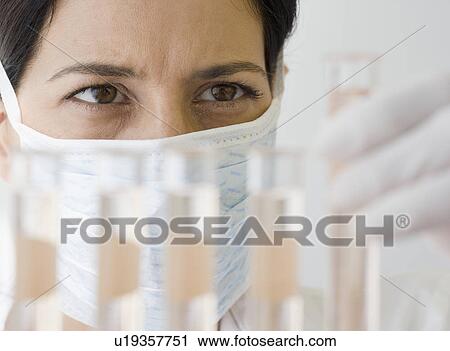 Stock Image - Female scientist looking at vials of liquid. Fotosearch