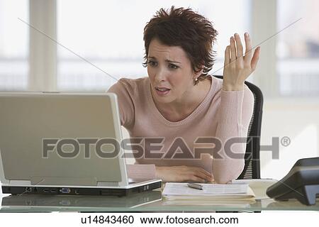 Stock Image - Frustrated businesswoman looking at laptop. Fotosearch