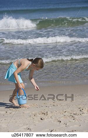 Stock Photo - Girl collecting shells at beach. Fotosearch