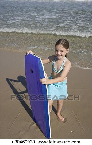 Stock Image - Girl holding boogie board at beach. Fotosearch