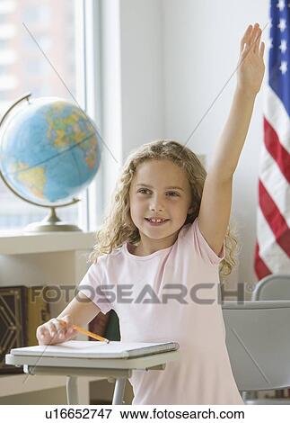 Stock Photo - Girl raising hand at school desk. Fotosearch