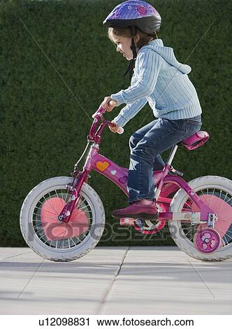 Stock Image - Girl riding bicycle with training wheels. Fotosearch