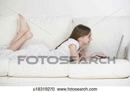 Stock Image - Girl using laptop on sofa. Fotosearch
