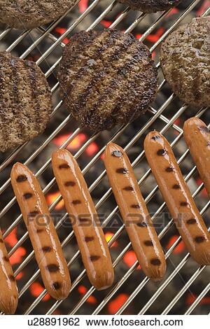 Stock Image - Hamburgers and hot dogs cooking on grill. Fotosearch