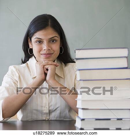 Stock Photo - Hispanic woman next to stack of school books. Fotosearch
